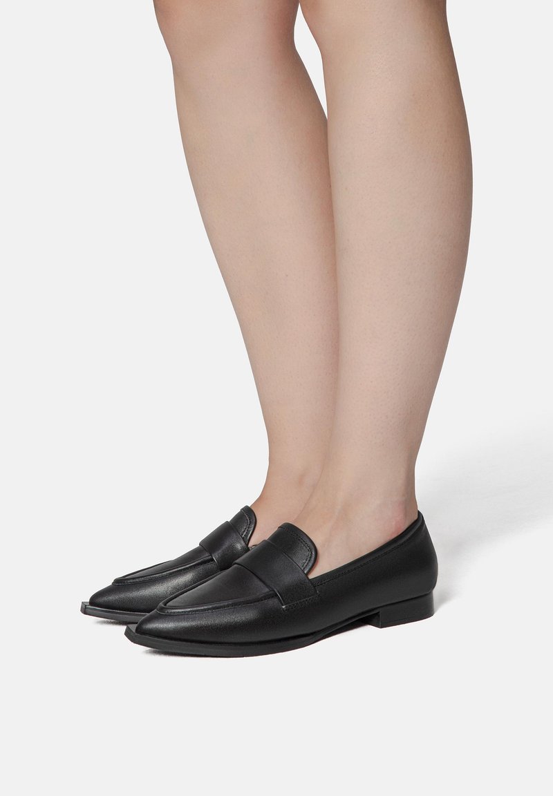 Black leather loafers with a pointed toe, flat sole, and a strap across the upper. Smooth texture and minimalist design.