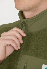 Olivenfarbene Fleecejacke mit glattem Obermaterial, strukturiertem unteren Teil, hohem Kragen und Reißverschluss-Taschen.