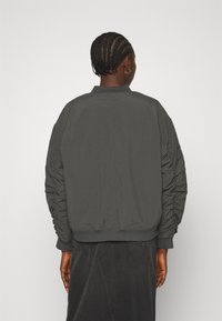 Giacca bomber grigia con colletto a coste e dettagli delle maniche arricciati. Tessuto liscio, con un orlo aderente e un design minimalista.