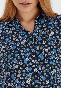 Blumenhemd mit knöpfen auf schwarzem Hintergrund und kleinen blauen, weißen und grünen Blumen. Mit Kragen und schwarzen Knöpfen.