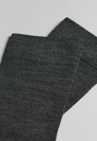 Dunkelgraue gestrickte Socken mit einer glatten Textur und gerippten Bündchen, die ein einfaches Design ohne Muster oder zusätzliche Akzente zeigen.