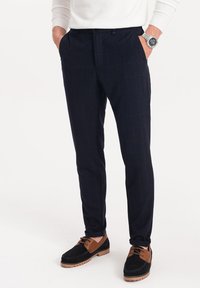 Marineblokkerige broek gemaakt van geweven stof, met zijzakken, een getailleerde pasvorm en een gladde textuur. Draag met zwart en bruine schoenen.