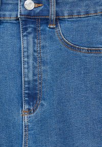 Tissu en denim bleu clair présentant deux poches avant, des coutures visibles de couleur orange, et une fermeture à bouton en métal brillant à la taille.