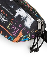 Černá taška s mnohobarevnými abstraktními vzory, se zipovým uzávěrem a texturovaným materiálem. Obsahuje značkovou etiketu s textem "Jean-Michel Basquiat".