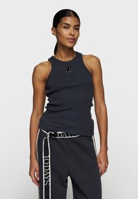 Marineblaues geripptes Tanktop mit Rundhalsauschnitt und ärmellosem Design; verfügt über ein kleines gesticktes Logo auf der Brust. Kombiniert mit grauen Sweatpants.