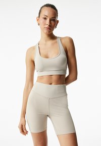 Soutien-gorge de sport beige et short taille haute en tissu extensible, présentant une texture lisse et des coutures minimales, conçu pour un usage actif.