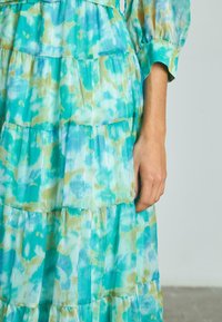 Abito maxi a strati in turchese e verde, con un motivo tie-dye, maniche lunghe e strati plissettati per una maggiore texture.