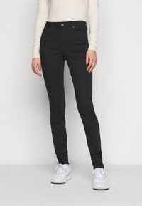 Jeans skinny negros hechos de una mezcla de algodón elástico, con cierre de botón, cinco bolsillos y una textura suave. Combinados con zapatillas blancas.