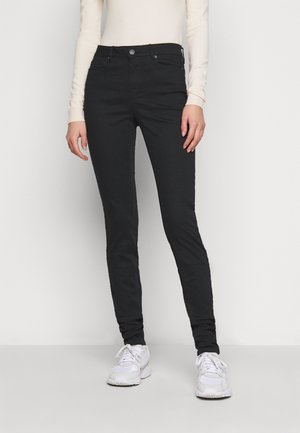 Jeans skinny negros hechos de una mezcla de algodón elástico, con cierre de botón, cinco bolsillos y una textura suave. Combinados con zapatillas blancas.