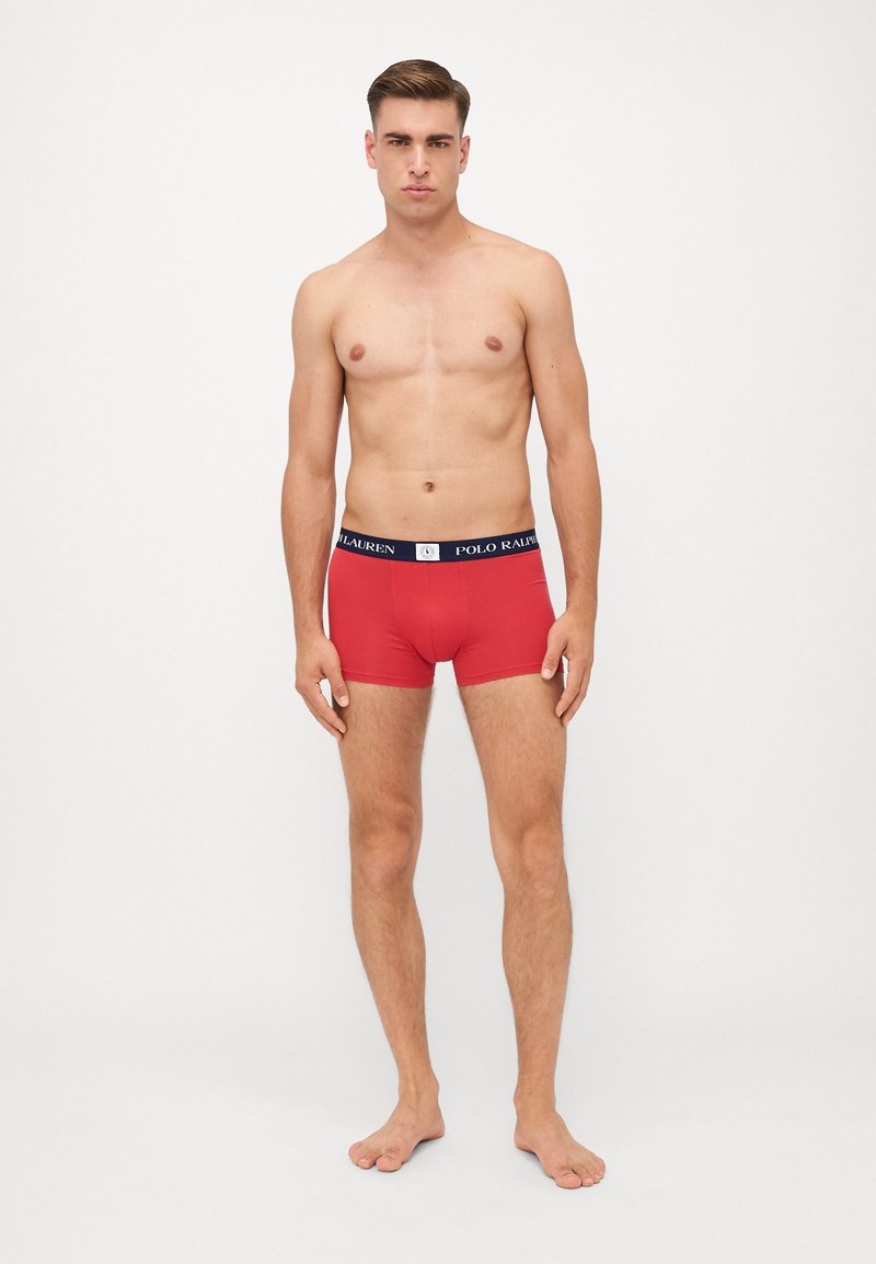 Boxeri roșii cu un tiv bleumarin pe care este inscripționat "POLO RALPH LAUREN." Materialul pare neted și elastic, aderând strâns de corp.