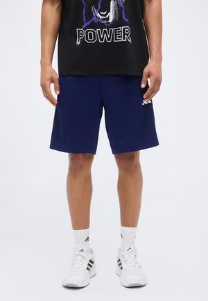 Uomo che indossa pantaloncini sportivi blu navy, scarpe e calzini Adidas bianchi e una maglietta nera con un leone ruggente e la scritta "POWER".