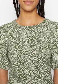 Zielony top w kwiatowy wzór z okrągłym dekoltem i krótkimi bufiastymi rękawami, wykonany z lekkiego materiału o teksturowanym wykończeniu.