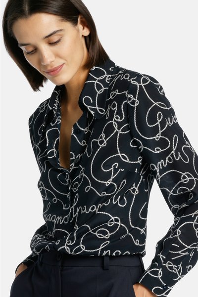 Blusa nera con stampa a corda bianca, dotata di colletto e chiusura frontale con bottoni. Tessuto liscio con silhouette attillata e maniche lunghe.