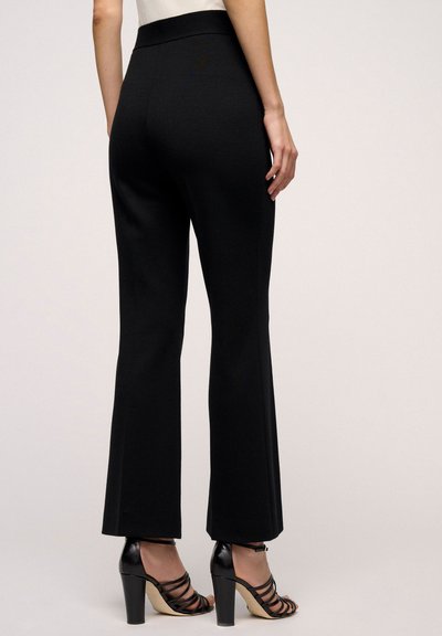Zwarte flared broeken met een gladde textuur, hoge tailleband en minimalistisch ontwerp. Gecombineerd met zwarte strappy heels met een stevige hak.