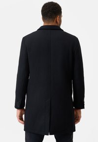 Black wool blend coat with a tailored fit, lapel collar, and two buttons on the sleeves. Straight cut, with a vented back design.