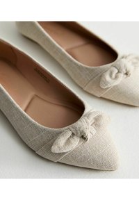 Ballerine beige a punta con texture intrecciata, caratterizzate da un fiocco decorativo sulla parte frontale e una fodera interna liscia. Immagine ravvicinata delle scarpe.