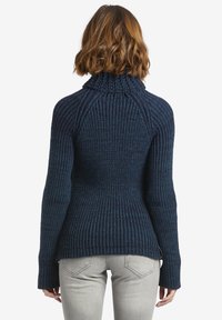 Tmavě modrý pletený svetr s vysokým límcem, žebrovanou texturou a přiléhavým střihem. Má dlouhé rukávy a mírné rozšíření v oblasti boků.
