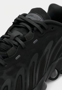 Sapatos atléticos pretos com parte superior sintética texturizada, apresentando um design moldado, atacadores visíveis e elementos de amortecimento proeminentes.