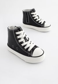 Baskets montantes noires en matériau synthétique, avec des lacets blancs, une semelle en caoutchouc blanche et des accents de coutures blanches. Fermeture éclair sur le côté.