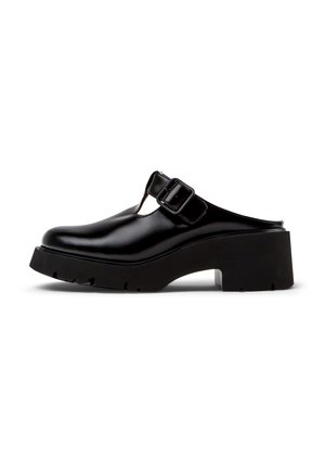 Zwarte leren slip-on mule met dikke hak, ronde neus, dikke zool en brede gespband over het bovenwerk.