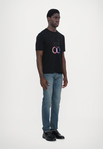 T-shirt noir à manches courtes avec un design graphique multicolore. Associé à un jean bleu clair et des chaussures noires.