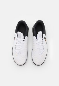 Weiße Sportschuhe mit schwarzen Akzenten und goldenem Logo, strukturiertem Obermaterial, kreisförmigem Muster und traditionellem Schnürsystem.