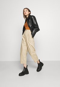 Veste en cuir noir courte sur un haut côtelé rouille, associée à un pantalon beige taille haute et des bottines Chelsea noires. Éléments de design simples.