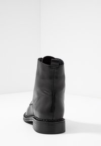 Bota de tobillo de cuero negro con textura suave, puntera redondeada y tacón bajo apilado. Cuenta con una tira de agarre para facilitar el uso.
