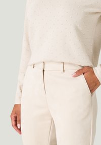 Cream-colored textured sweater with raised dots, paired with light beige, smooth suede-like pants featuring side pockets and a fitted waist.