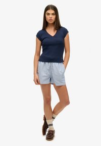 Marineblauw ribbelshirt met korte mouwen en kantafwerking, gecombineerd met blauw-witte gestreepte shorts. Bruine schoenen en lichtgekleurde sokken maken de look compleet.