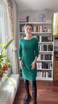 Zaļa pieguļoša kleita ar garām piedurknēm un krokām, kombinēta ar līdz ceļiem melniem mākslīgās ādas zābakiem. Minimālistisks dizains, gluda auduma tekstūra.