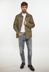 Olivgrön lättviktsjacka med fyra framfickor, knäppning framtill och krage. Matchad med blekta grå jeans och svarta stövlar.