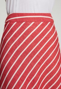 Jupe à rayures rouges et blanches en tissu texturé, dotée d'une taille ajustée et de lignes diagonales qui créent un intérêt visuel.