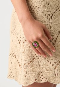 Green resin ring with a pink gem, square shape. Hand wearing the ring features a natural nail finish, paired with a crocheted beige dress.