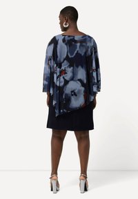 Vestido fluido de color azul marino con estampado floral en tonos azules y rojos. Presenta mangas anchas, parte trasera en capas y una falda ajustada. Tacones plateados.