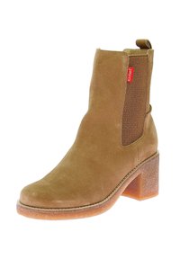 Botín de ante marrón con un inserto de malla texturizada y tacón ancho. Cuenta con una pequeña lengüeta para tirar y costuras visibles a lo largo de la suela.