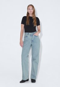 Jeans de mezclilla de tiro alto en un tono azul claro, con un corte relajado, bolsillos frontales y un efecto de desvanecimiento. Combinados con una camiseta negra ajustada de manga corta.