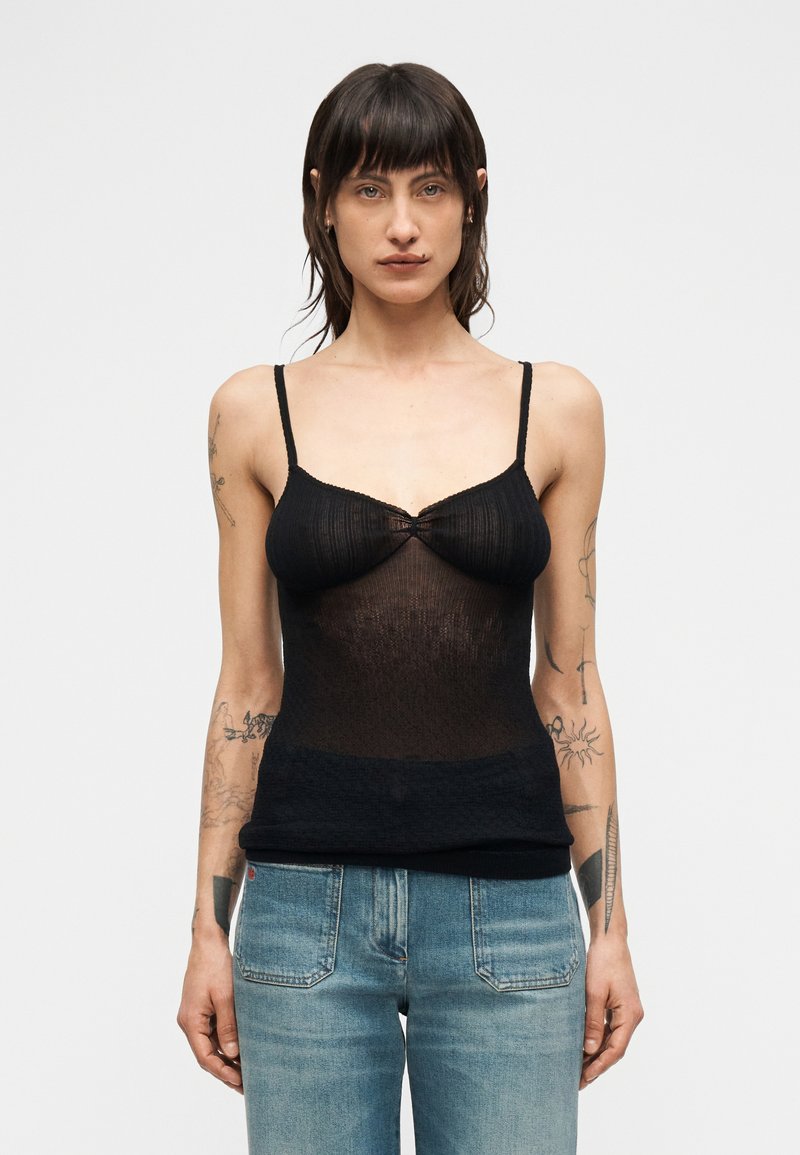 Μαύρο ημιδιαφανές τοπ με λεπτές τι ράντες, με υφή ριμπ και λεπτομέρεια συγκέντρωσης στο κέντρο του στήθους. Συνδυασμένο με ανοιχτόχρωμο μπλε τζιν.