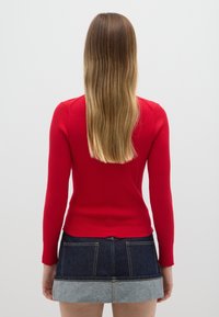 Rode ribgebreide trui met lange mouwen, nauwsluitend model. Gecombineerd met een denim minirok met een lichte denim zoom en achterzakken.