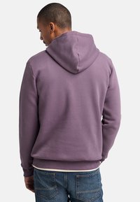 Felpa con cappuccio viola dal tessuto morbido, con polsini aderenti e una tasca frontale a marsupio, abbinata a jeans blu.