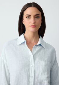 Lichtblauwe linnen shirt met een traditionele kraag, lange mouwen, knoopsluiting aan de voorkant en een borstzak; zachte textuur en een ontspannen pasvorm.