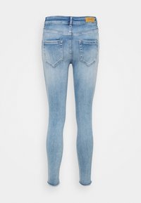 Jean skinny bleu clair avec poches arrière, ourlets effilochés et une petite étiquette beige de la marque sur la ceinture, sur fond blanc.
