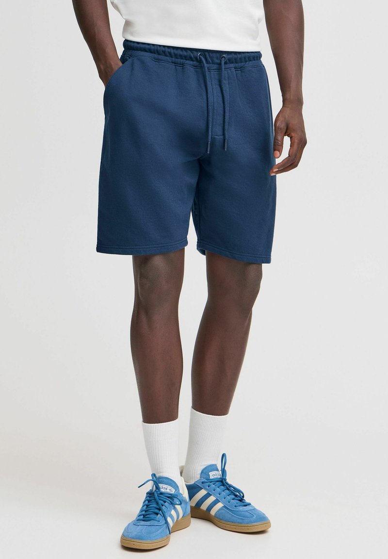 Marineblå bomuldsshorts med elastisk talje og snor, med sidelommer og en afslappet pasform. Bæres med blå sneakers og hvide sokker.