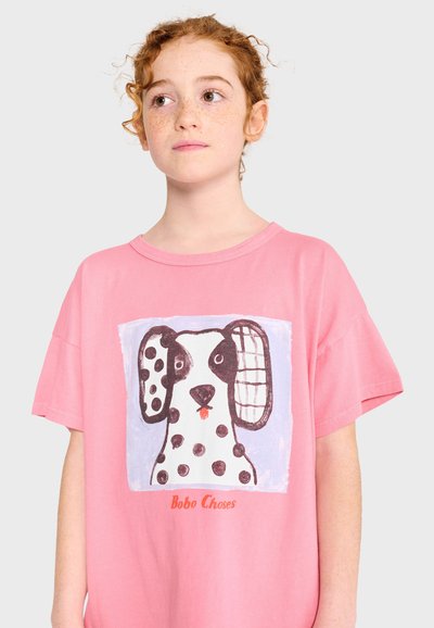 Red-haired child wearing a pink T-shirt with a black and white spotted dog illustration and "Bobo Choses" text.