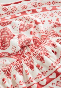 Rot-weißer gemusterter Stoff mit Herzen, Vögeln und floralen Motiven. Weiche Textur mit einem gerafften Taillenbund.
