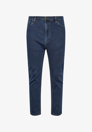 Hand in einer blauen Jeanstasche, mit einem dunkelblauen Strickshirt, das locker über dem Bund liegt, in Nahaufnahme.