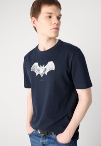 Námořnická modrá bavlněná tričko s velkým bílým potiskem netopýra a textem "BOSS" umístěným centrálně pod designem. Krátké rukávy a kulatý výstřih.