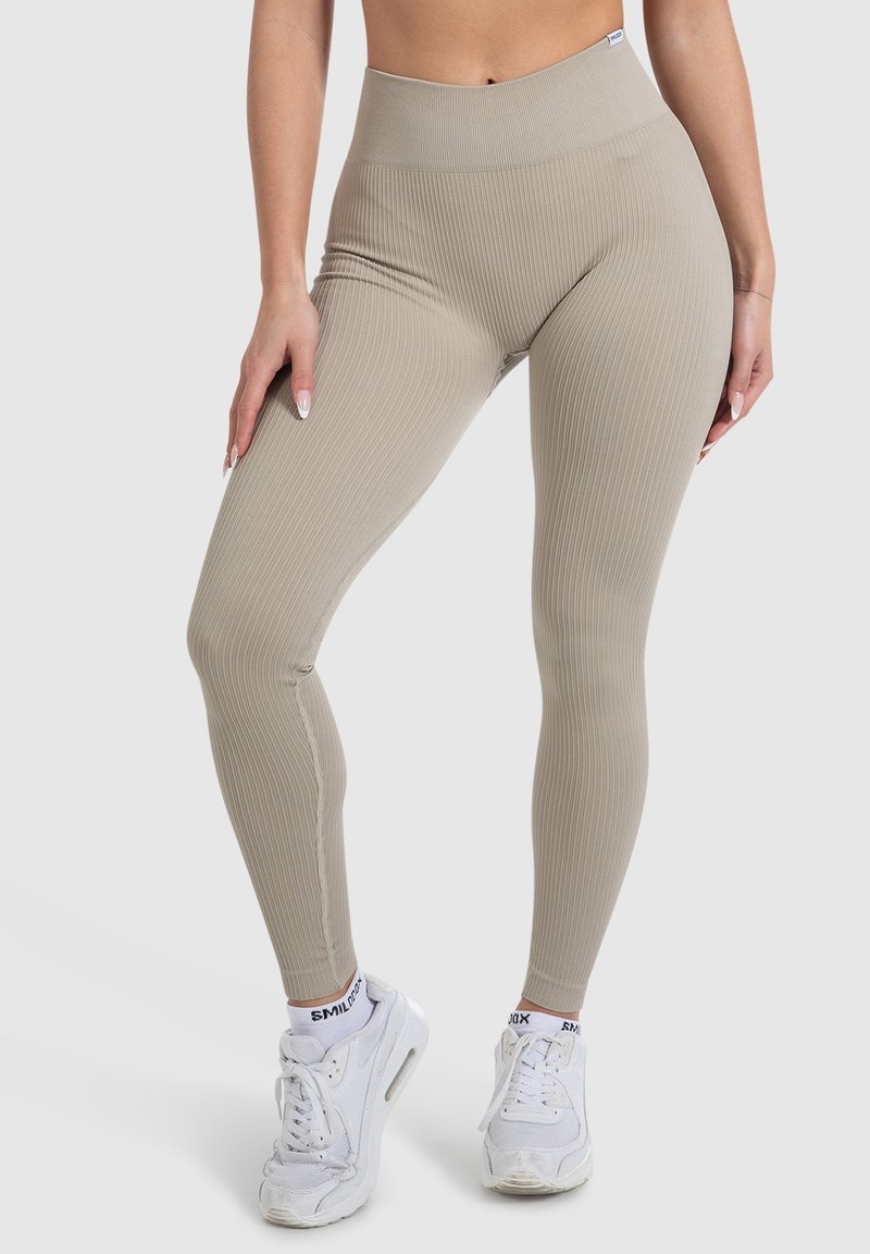 Beige geribbelde leggings met een hoge tailleband en een snug fit, gemaakt van rekbaar materiaal. Gecombineerd met witte sneakers en gestreepte sokken.