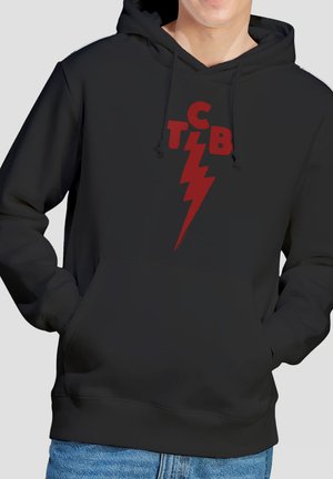 Person trägt schwarzen Hoodie mit roten Buchstaben "CTIB" und Blitzdesign, die Hände in der vorderen Tasche, kombiniert mit blauer Jeans.