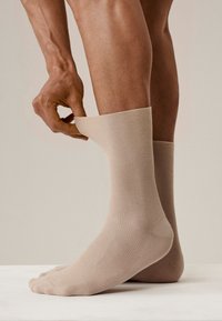 Beżowe skarpety z prążkami podciągane, ukazujące gładką fakturę i dopasowany krój. Stopa jest częściowo widoczna, podkreślając kolor i wzór.